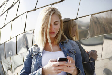 Deutschland, Düsseldorf, lächelnde blonde Frau schaut auf ihr Smartphone vor einer modernen Fassade - RHF000860