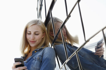 Deutschland, Düsseldorf, Porträt einer lächelnden blonden Frau mit Blick auf ihr Smartphone - RHF000844