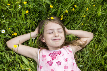 Porträt eines lächelnden kleinen Mädchens mit geschlossenen Augen, das auf einer Blumenwiese liegt - SARF001776