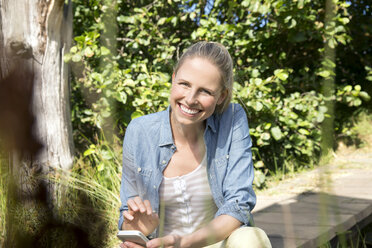 Smiling woman with cell phone in rural landscape - TOYF000351