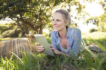 Lächelnde Frau mit digitalem Tablet auf einer Wiese liegend - TOYF000360