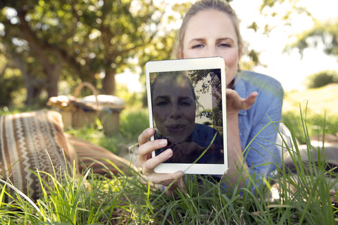 Frau mit digitalem Tablet auf einer Wiese liegend, die ein Selfie zeigt - TOYF000361