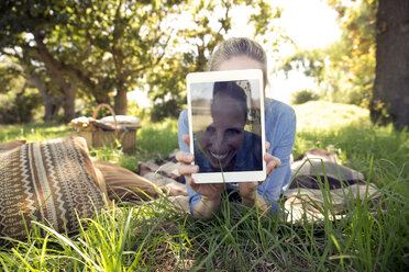 Frau mit digitalem Tablet auf einer Wiese liegend, die ein Selfie zeigt - TOYF000362