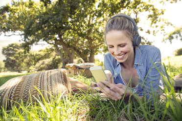Smiling woman lying on meadow listening to music from smartphone - TOYF000366