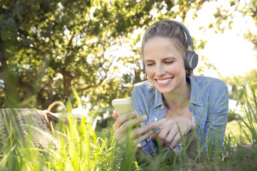 Lächelnde Frau liegt auf einer Wiese und hört Musik vom Smartphone - TOYF000368