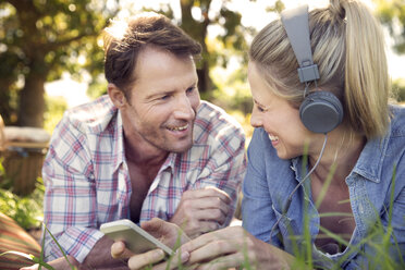 Glückliches Paar auf der Wiese liegend, Frau hört Musik vom Smartphone - TOYF000371