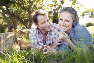 Glückliches Paar auf der Wiese liegend, Frau hört Musik vom Smartphone - TOYF000373