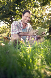 Lächelnder Mann mit digitalem Tablet auf einer Wiese sitzend - TOYF000383