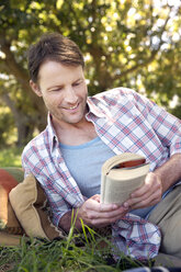 Lächelnder Mann liegt auf einer Wiese und liest ein Buch - TOYF000391