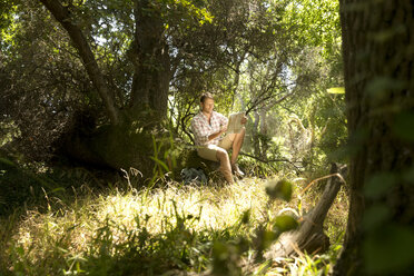 Hiker sitting on tree trunk reading map - TOYF000404