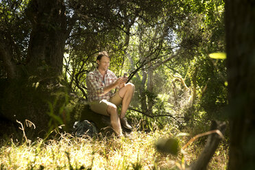 Hiker sitting on tree trunk reading map - TOYF000405