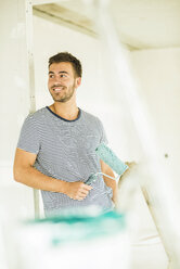 Smiling young man renovating holding paint roller - UUF004162