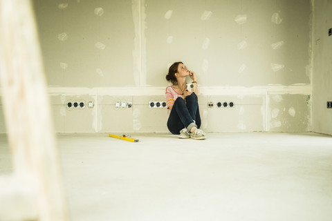 Junge Frau beim Renovieren an einer leeren Wand sitzend, lizenzfreies Stockfoto