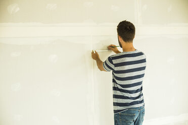 Young man renovating drawing marking at wall - UUF004179