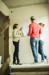 Architect showing construction plan to young couple - UUF004200