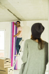 Young man renovating showing wallpaper to woman - UUF004221