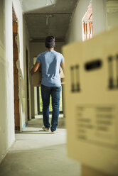 Young man carrying cardboard box in hallway - UUF004233