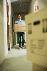 Young man carrying cardboard box in hallway - UUF004234