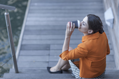 Frau sitzt auf Stufen und trinkt Kaffee, lizenzfreies Stockfoto