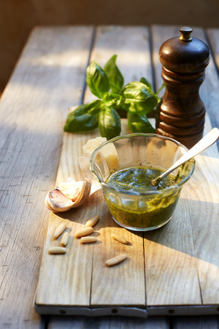 Ein Glas hausgemachtes Basilikum-Pesto, Zutaten und eine Pfeffermühle, lizenzfreies Stockfoto