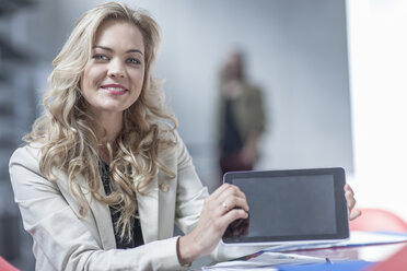 Portrait of smiling young businesswoman showing mini tablet - ZEF005054