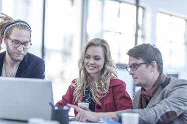 Three colleagues looking at laptop in an office - ZEF005089