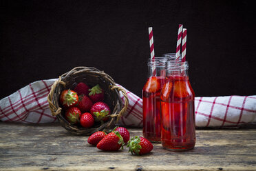 Drei Glasflaschen mit selbstgemachter Erdbeerlimonade und ein Weidenkorb mit Erdbeeren - LVF003361
