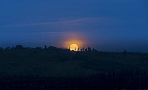 Italien, Toskana, Val d'Orcia, Monduntergang hinter Zypressen, lizenzfreies Stockfoto