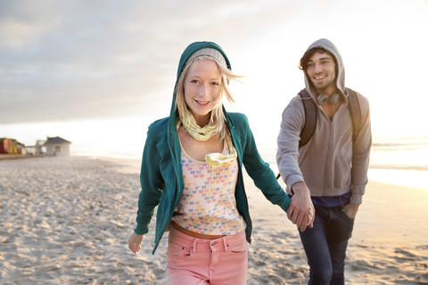 Junges Paar geht bei Sonnenaufgang am Strand spazieren, lizenzfreies Stockfoto