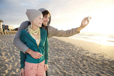 Young couple taking a selfie on beach at sunrise - TOYF000415