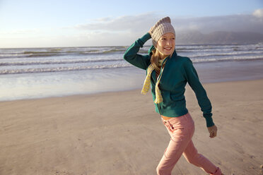 Smiling young woman walking on beach - TOYF000428