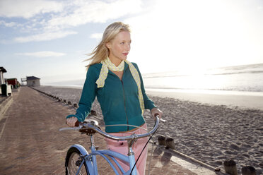 Lächelnde junge Frau mit Fahrrad an der Strandpromenade - TOYF000434