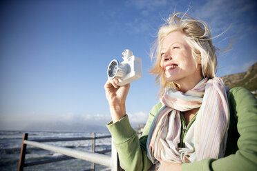 Lächelnde junge Frau an der Küste beim Fotografieren - TOYF000437