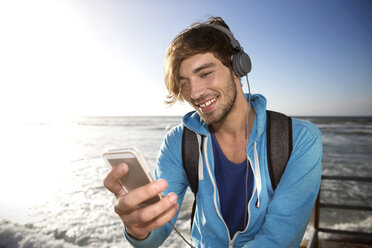 Glücklicher junger Mann an der Küste, der mit seinem Smartphone Musik hört - TOYF000445