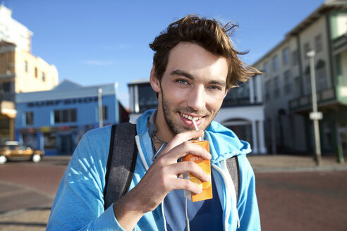 Porträt eines lächelnden jungen Mannes, der aus einem Saftkarton trinkt - TOYF000448