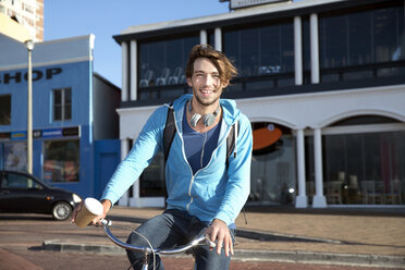 Lächelnder junger Mann mit Kaffee in der Hand zum Mitnehmen auf dem Fahrrad - TOYF000451
