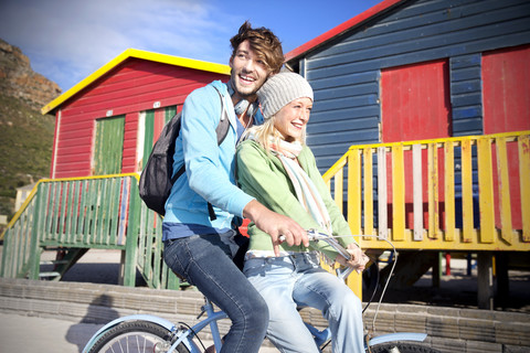 Junges Paar fährt Fahrrad an bunten Strandhütten, lizenzfreies Stockfoto