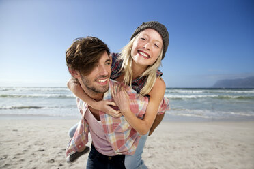 Young man carrying girlfriend piggyback on beach - TOYF000484