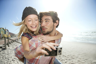 Junge Frau auf dem Rücken ihres Freundes am Strand macht ein Selfie - TOYF000488