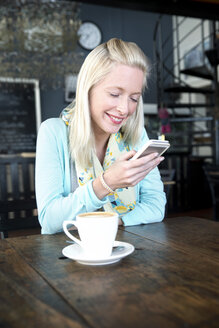 Junge Frau in einem Café schaut auf ihr Handy - TOYF000510