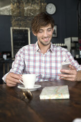 Lächelnder junger Mann in einem Café, der auf sein Handy schaut - TOYF000517