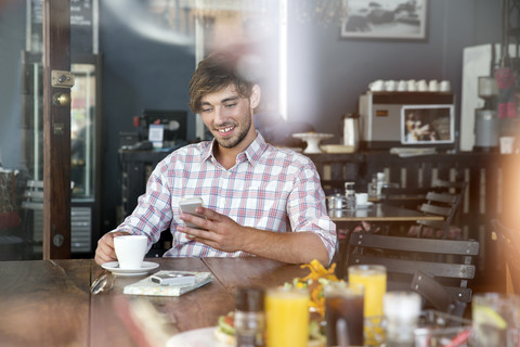 Lächelnder junger Mann in einem Café, der auf sein Handy schaut, lizenzfreies Stockfoto