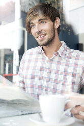 Lächelnder junger Mann in einem Café mit Blick nach oben - TOYF000520