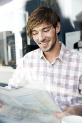 Smiling young man in a cafe reading newspaper - TOYF000522