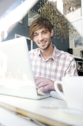 Lächelnder junger Mann in einem Café mit Laptop - TOYF000524