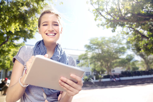 Lächelnde junge Frau, die im Freien ein digitales Tablet benutzt - TOYF000530