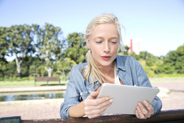 Young woman using digital tablet on park bench - TOYF000561