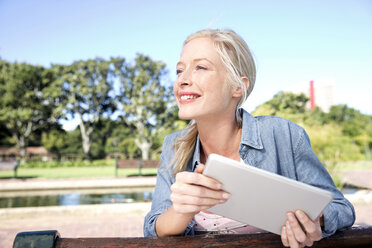 Young woman using digital tablet on park bench - TOYF000562