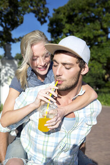 Junger Mann trinkt Erfrischungsgetränk und trägt seine Freundin Huckepack - TOYF000579