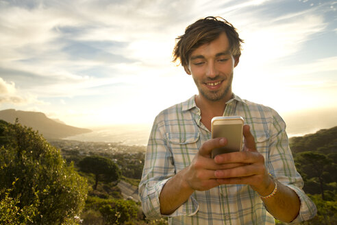 Junger Mann an der Küste mit Mobiltelefon - TOYF000589